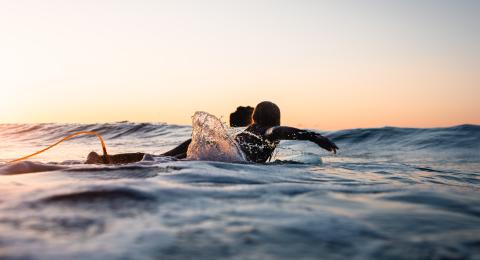 Surfer on surf board riding low waves as the sun comes up