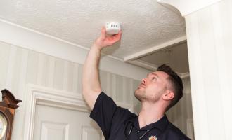 Fire Safety Officer fitting smoke alarm on ceiling