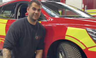 Tom Reed, an Engineer in our Fleet Workshops, in front of a red and yellow fire car. 