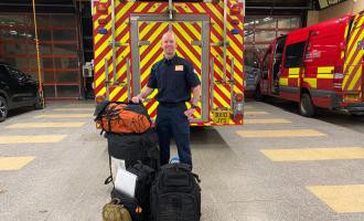 Firefighter Rob Thomson standing in front of a fire engine with his bags, ready to fly to Malawi