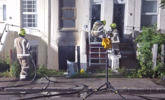 Firefighters outside a terraced house, with heat damage visible on a window