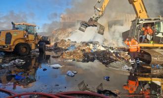 A smouldering pile of rubbish being broken up by a digger