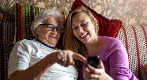 Young lady smiles at phone together with older lady