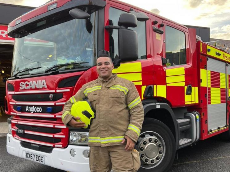 Dominic Daniel, on-call firefighter, stands in front of a fire engine.