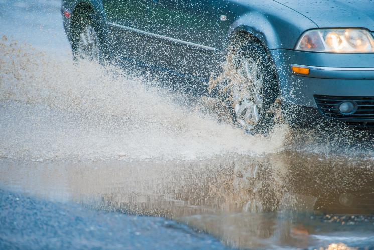 Teal car driving through large puddle