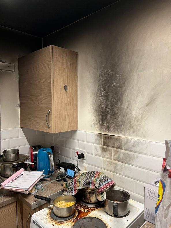 A kitchen with a scorched wall behind the cooker