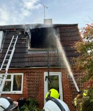 Firefighters spraying water onto the roof of a fire damaged house