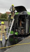 Burnt out bus and two firefighters using a ladder 