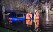 Two firefighters in water up to their waist looking into a flooded car