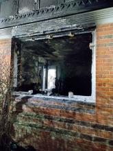 Looking into the burnt interior of the house through a window frame