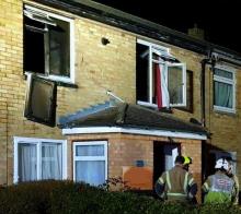 Firefighters outside the terraced house, with windows blown out