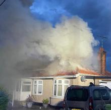Smoke billowing out of the roof of a bungalow